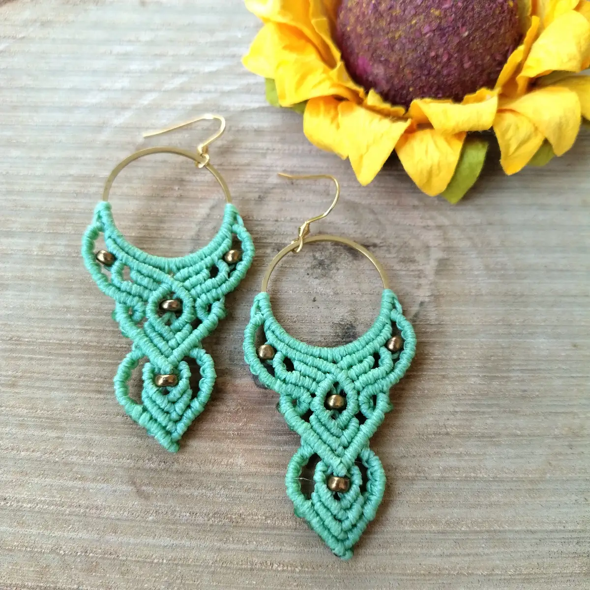 Χειροποίητα μακραμέ σκουλαρίκια Mint Flow earrings σε χρώμα μέντας με περίτεχνη πλέξη, χρυσά ατσάλινα στοιχεία και κούμπωμα τοποθετημένα σε ξύλινη επιφάνεια.